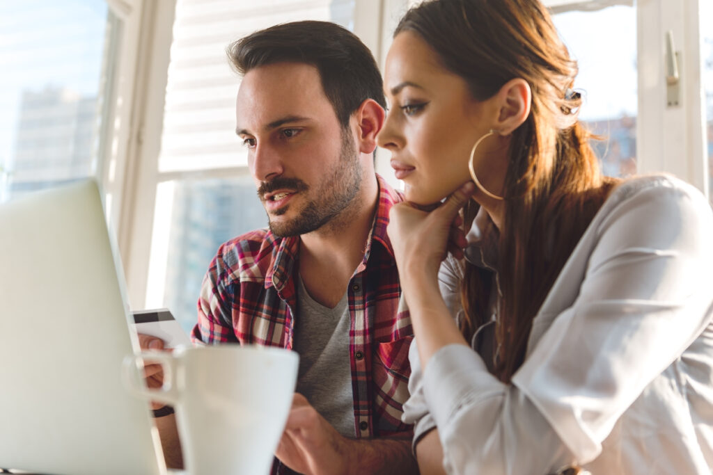 Una pareja está sentada en una mesa hablando mientras usa la computadora. La mujer está pensativa mientras el hombre estudia los mejores programas de fidelización para ganar y vender millas aéreas de forma segura
