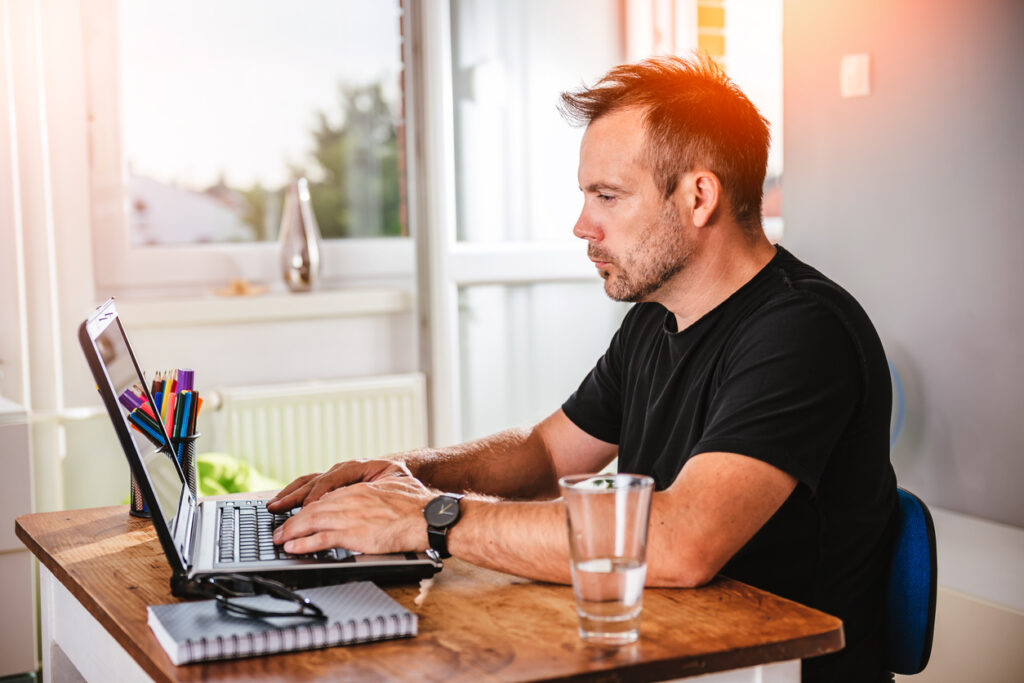 Un hombre blanco con cabello gris y una camisa negra está sentado en una mesa trabajando en su computadora. Está pensativo mientras aprende sobre las leyes que protegen a las millas y su comercio